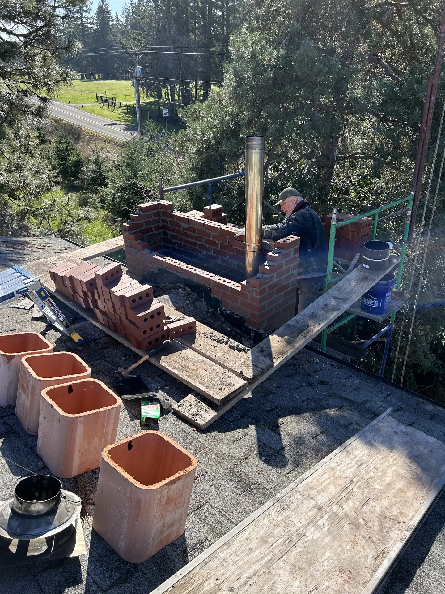 A First Rate Chimney mason rebuilding a brick chimney on a rooftop scaffold