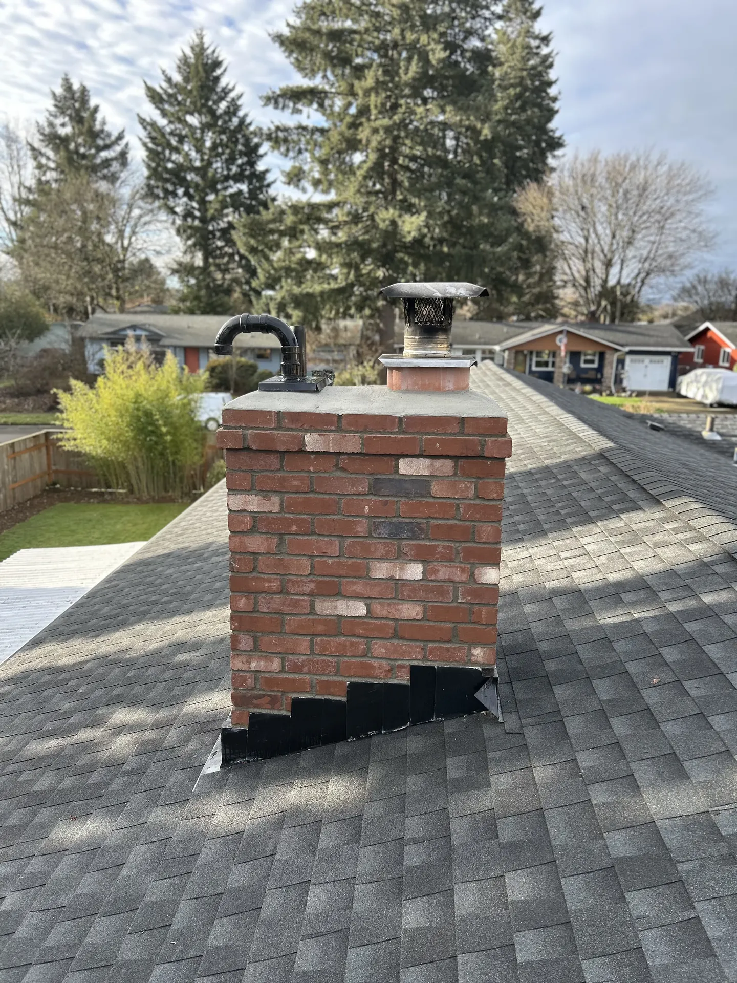 A First Rate Chimney technician sweeping a brick chimney from the rooftop in Estacada, Oregon