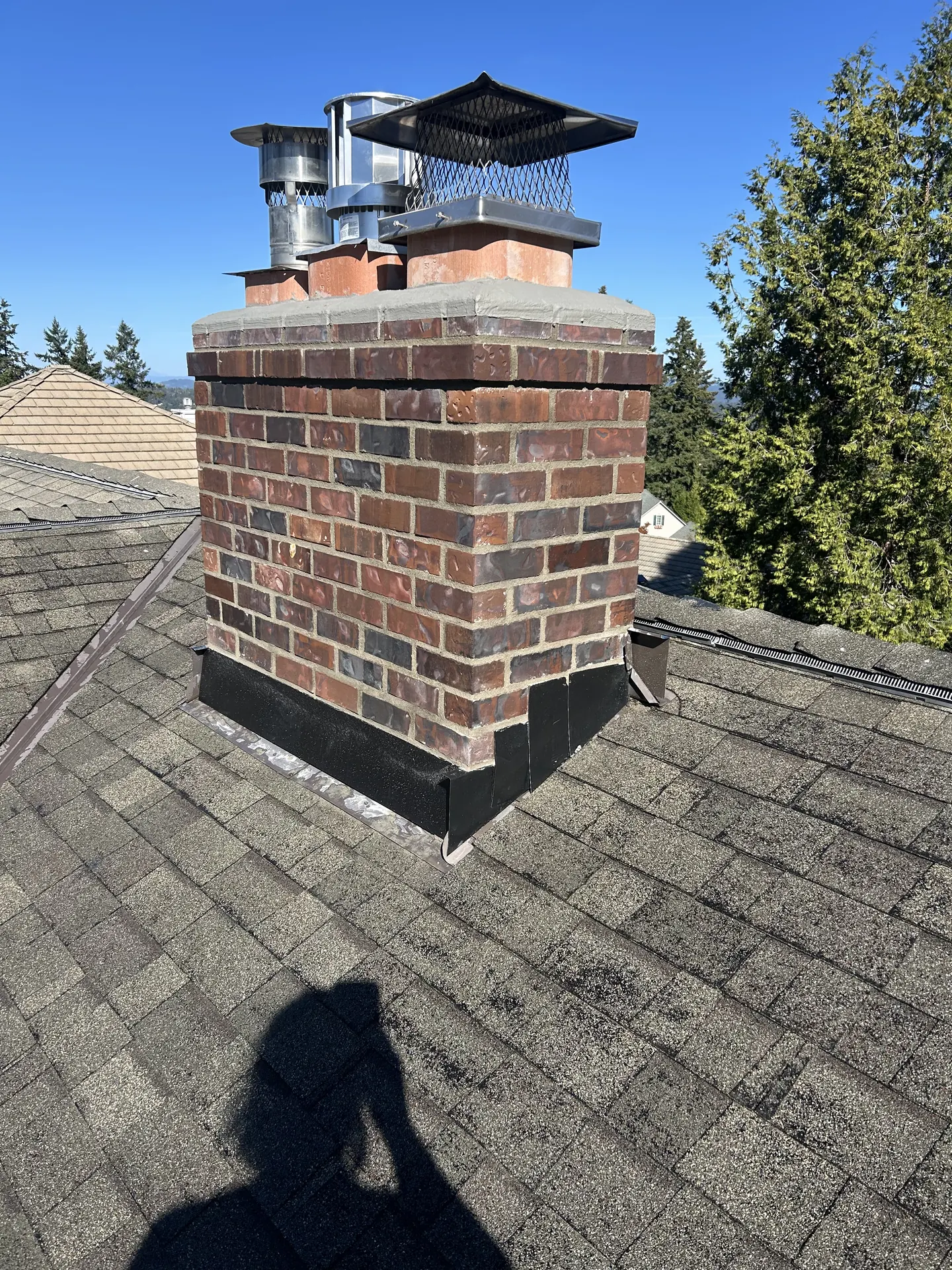 Gas fireplace venting and custom caps on a dark brick chimney installed by First Rate Chimney